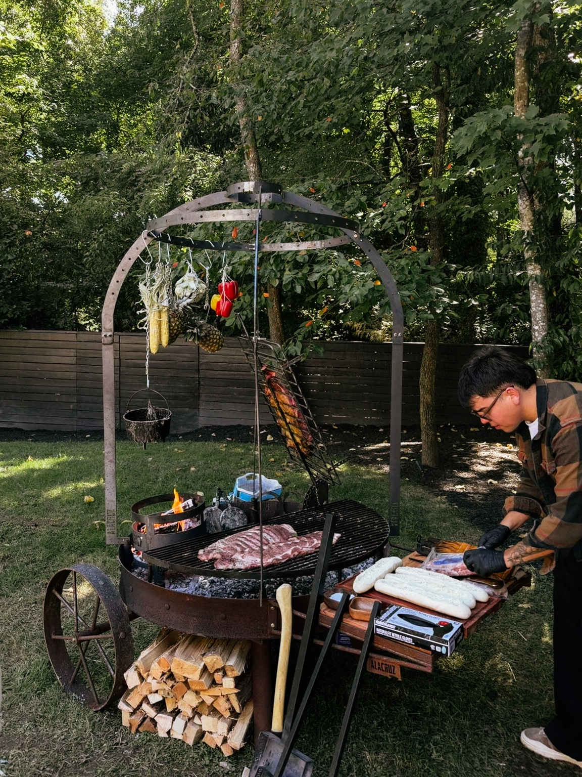 Fire Heritage cooking outdoors on a wood-fired grill, with hanging vegetables and meat roasting over the embers